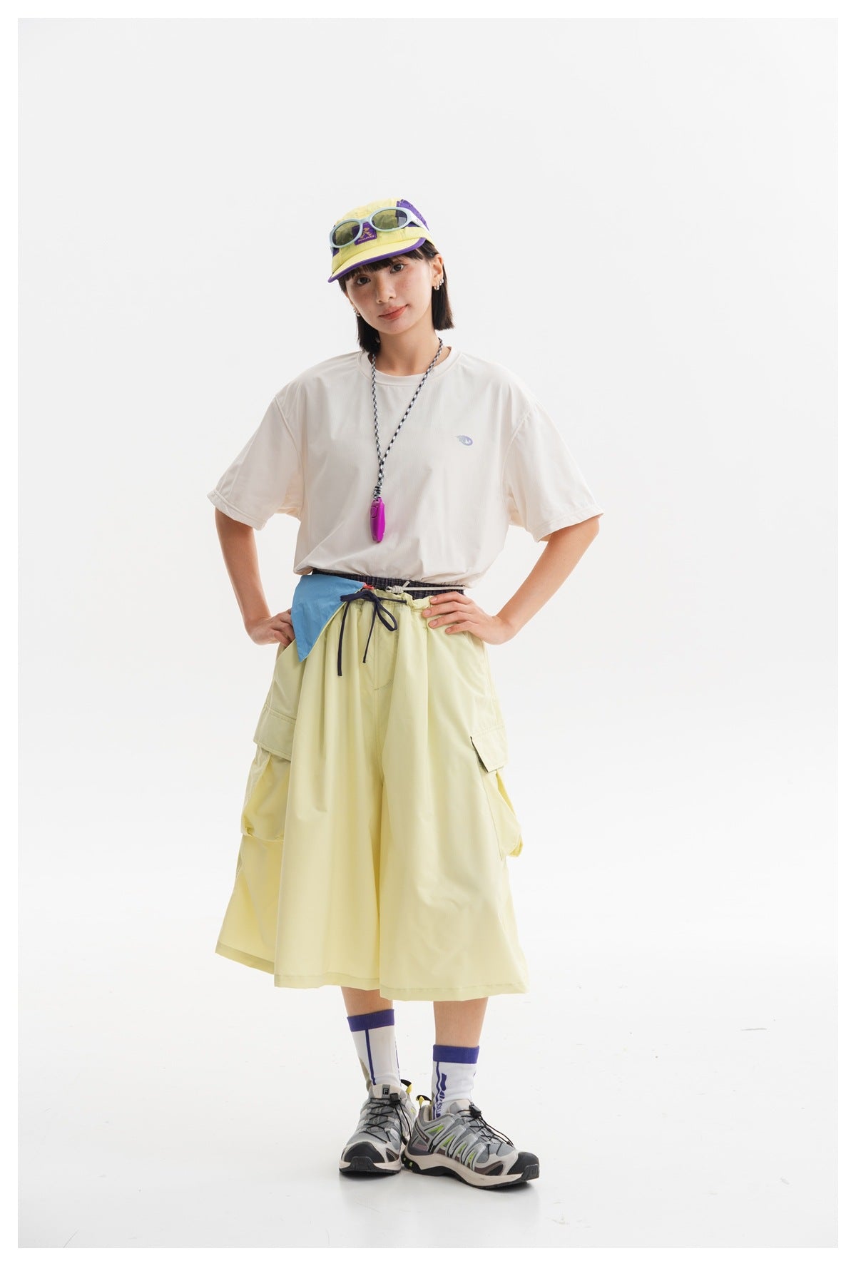Model wearing a pale yellow flared cargo skirt with large side pockets and a dark drawstring waist.