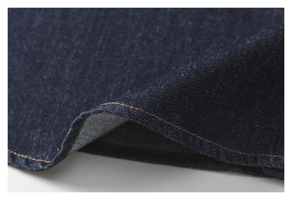 Close-up of a curved dark indigo denim edge with tan stitching and the lighter underside visible.
