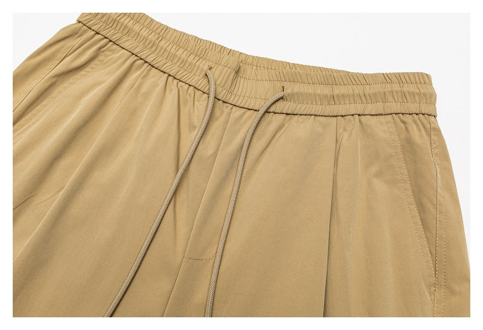 Close-up of tan pants showing an elastic waistband, drawstring, and front pocket seam.