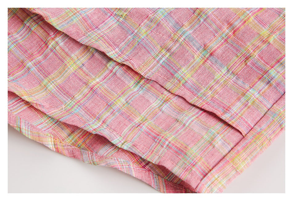 Close-up of pink plaid fabric with pastel stripes and a stitched folded edge.