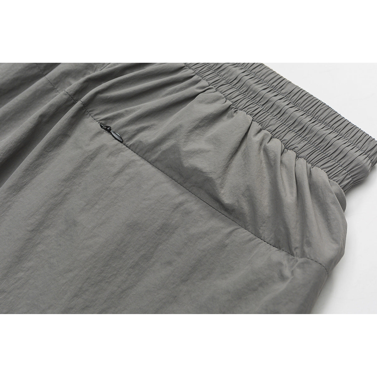 Close-up of gray shorts showing a slanted pocket opening beside the gathered elastic waistband.