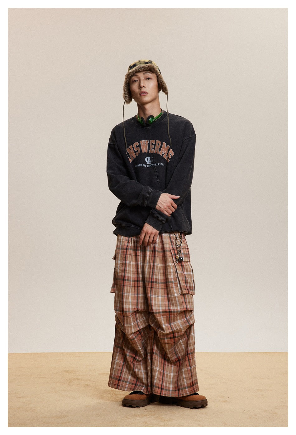 Model with arms folded wearing black washed ANSWERME sweatshirt with plaid cargo pants and fleece-trim hat