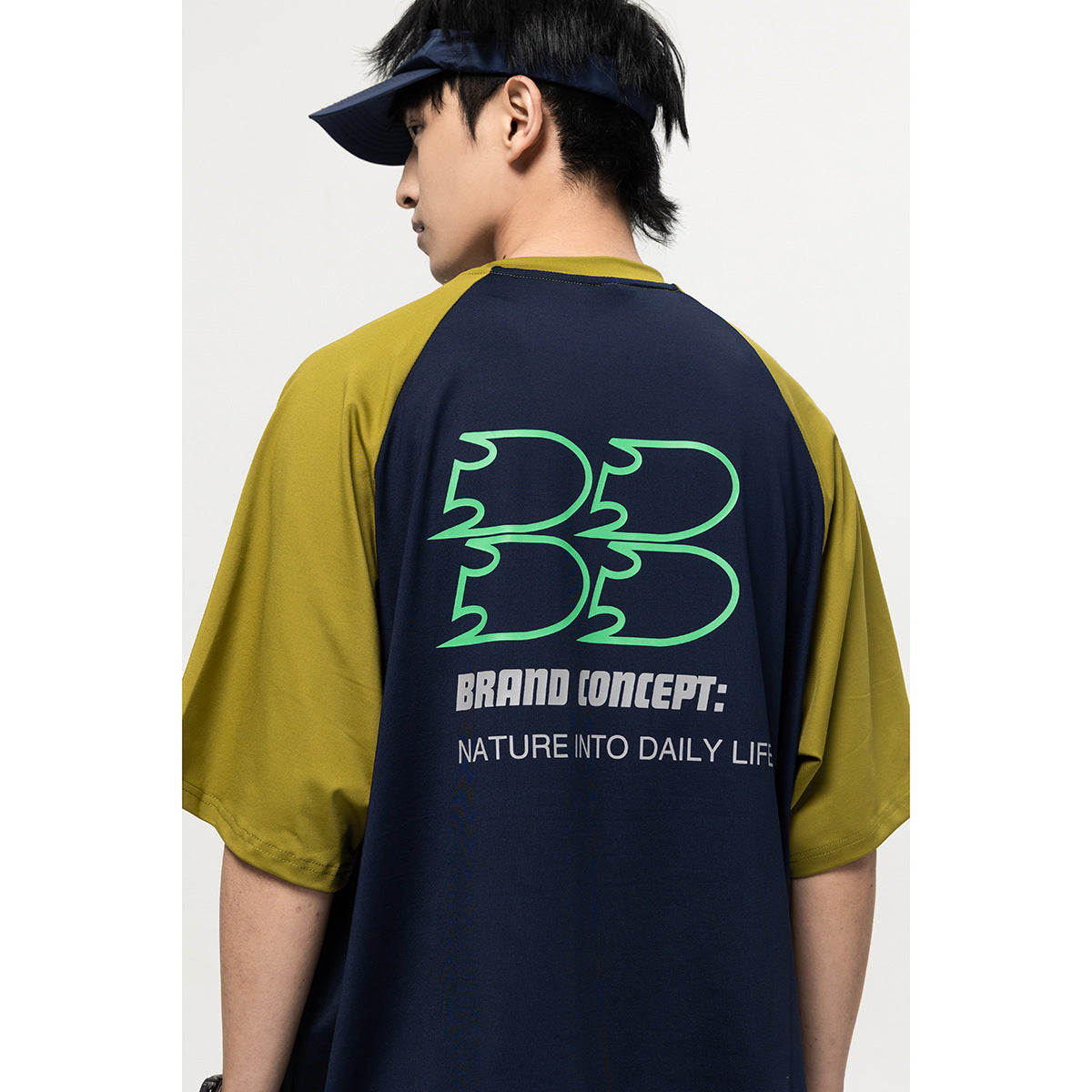 Back view of a model wearing a navy raglan T-shirt with olive sleeves and a large green-and-white graphic.