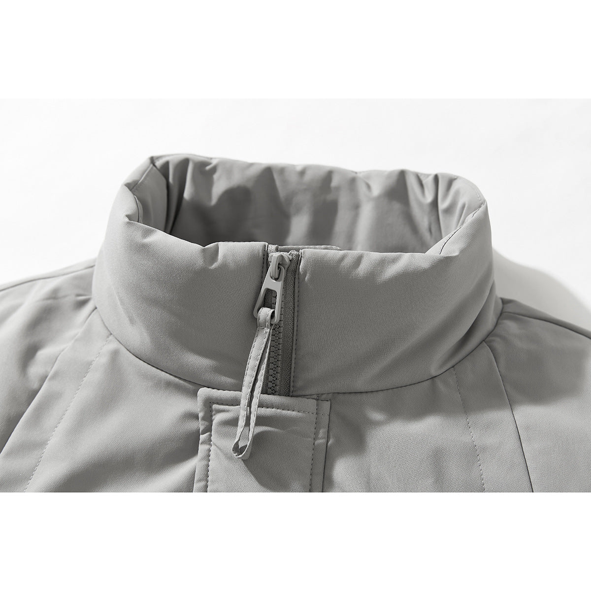 Close-up of a light gray jacket's tall stand collar, front zipper, and hanging zipper pull.