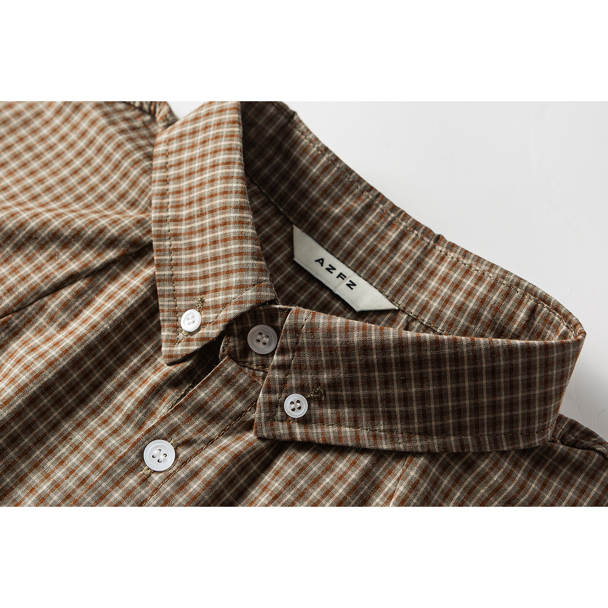 Close-up of a brown plaid short-sleeve shirt collar, white buttons and inner neck label.