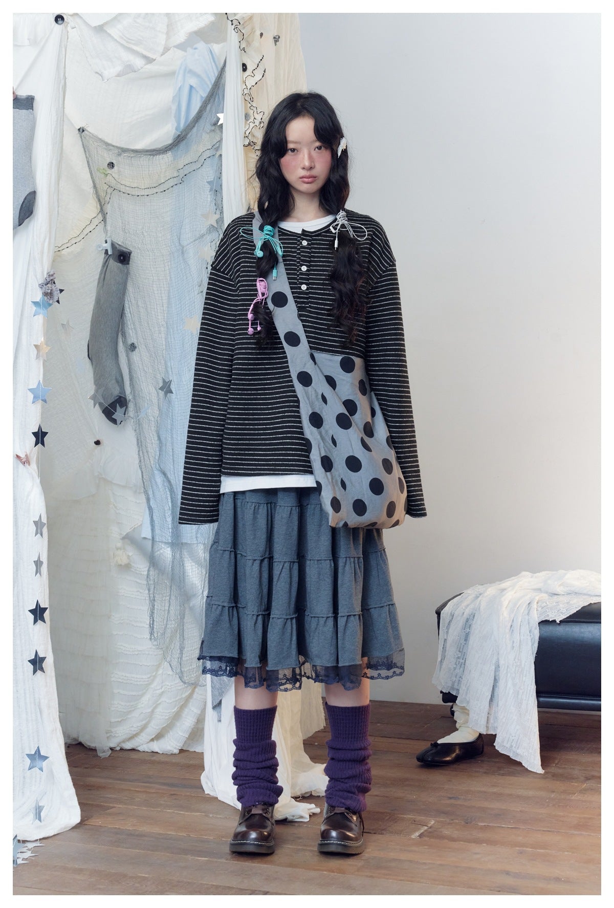 Model wearing a black-and-white striped button-front top and charcoal tiered skirt with lace hem, carrying a gray polka-dot