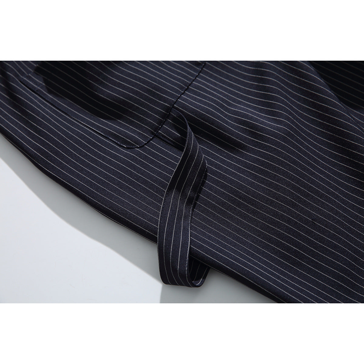 Close-up of dark pinstripe shorts showing a pocket seam and a narrow matching fabric tab.
