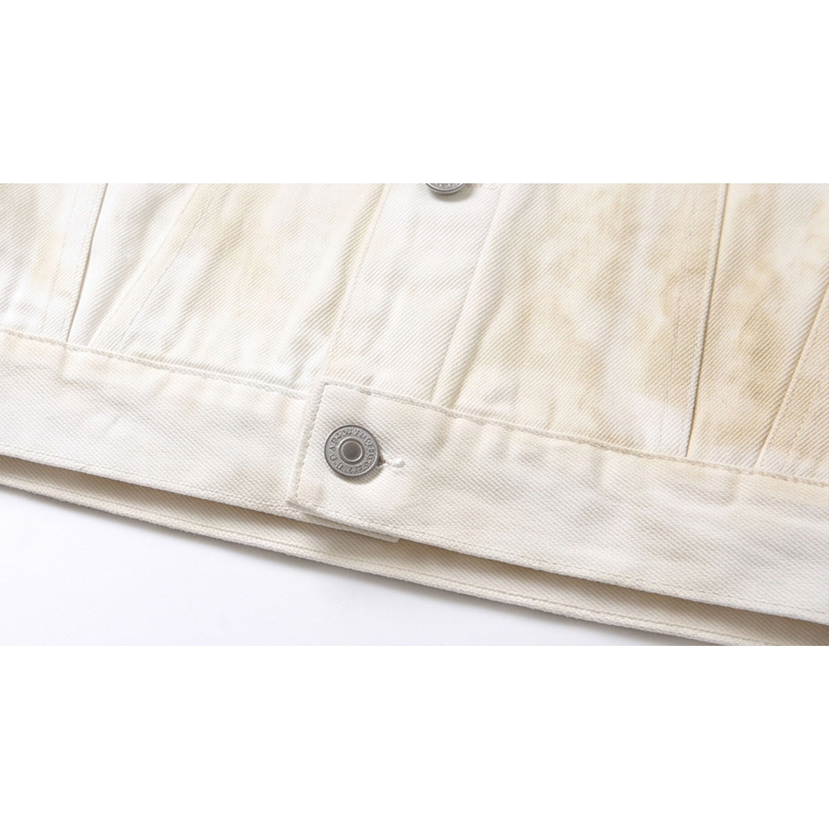 Close-up of an ivory jacket hem with a metal button and visible seam stitching.