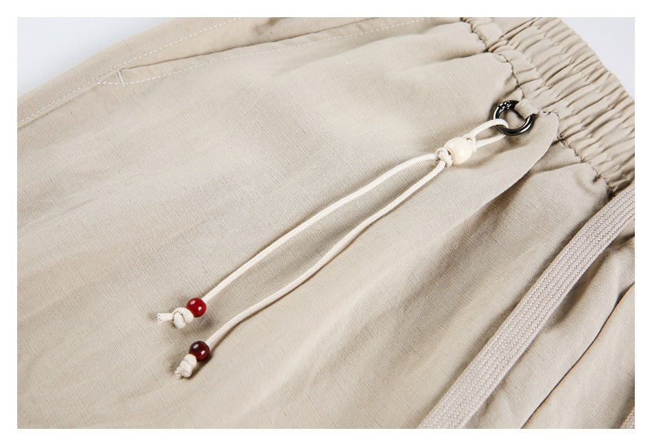 Close-up of beige pants with a drawstring cord, beads, metal loop, and elastic waistband.
