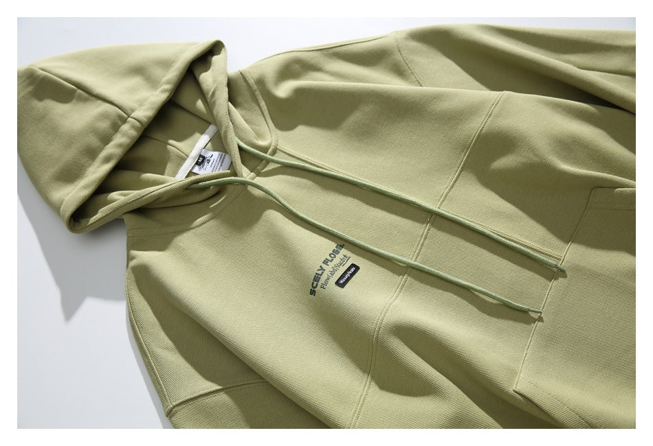 Close-up of the olive-green hoodie front, showing its hood, drawstrings, seams, and small chest print.