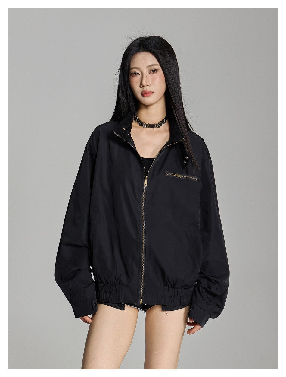 Model wearing a black zip-front jacket with the collar open, showing a black top and chest zip pocket.