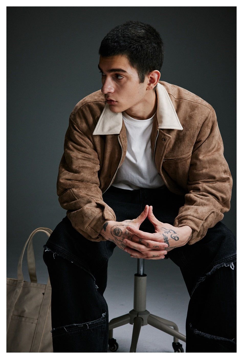 Seated model wearing a tan jacket with a wide cream collar and zip chest pocket.