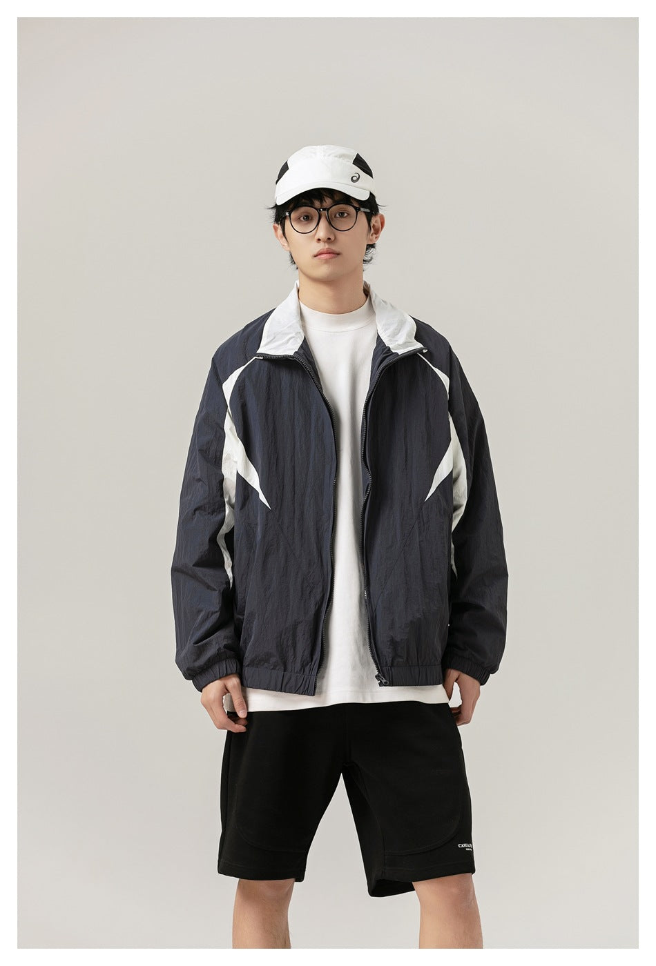 Front view of a model wearing an open dark jacket with white panels over a white shirt and black shorts.