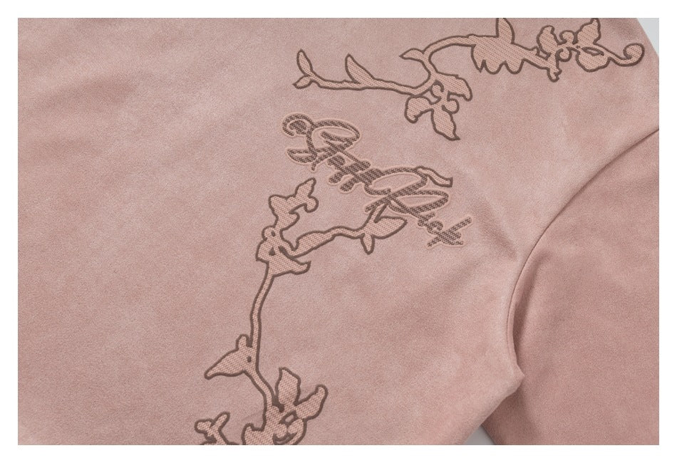 Close-up of dusty pink fabric with embroidered floral vines and decorative script.