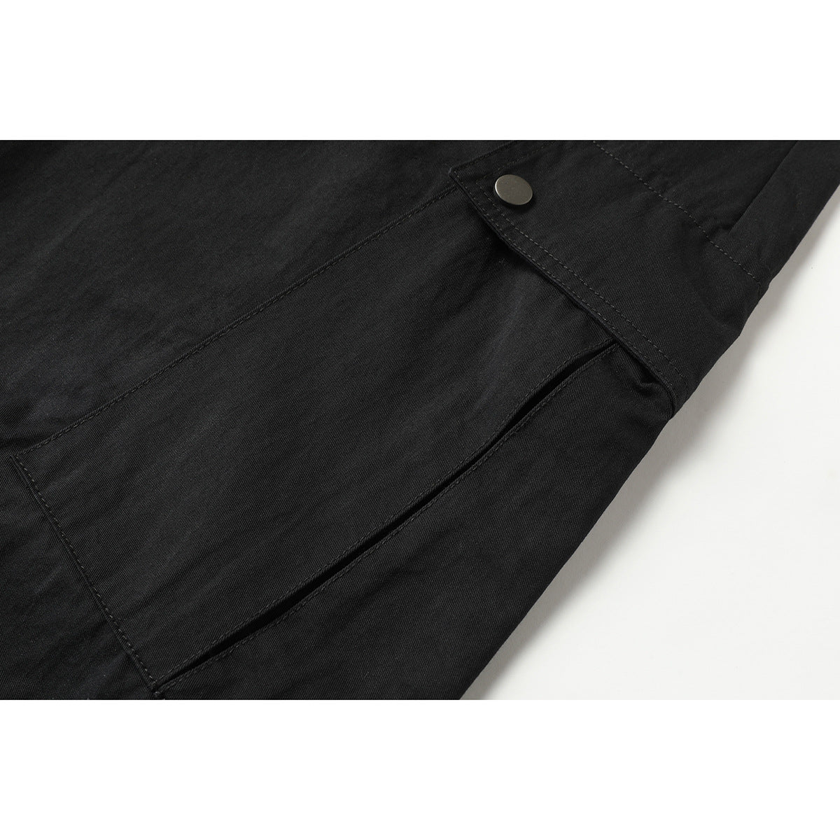 Close-up of black pants showing a flap cargo pocket with a metal snap and stitched seams.