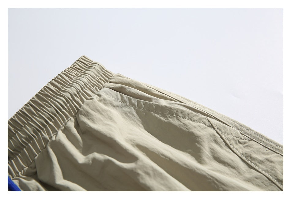 Close-up of beige trousers showing the gathered elastic waistband, seams, and wrinkled fabric.