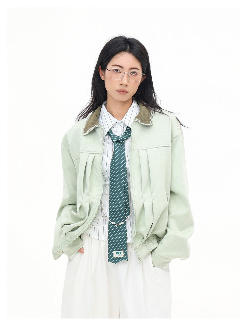 Waist-up front view of a model wearing an open pale mint jacket with a contrasting collar and pleated front details.