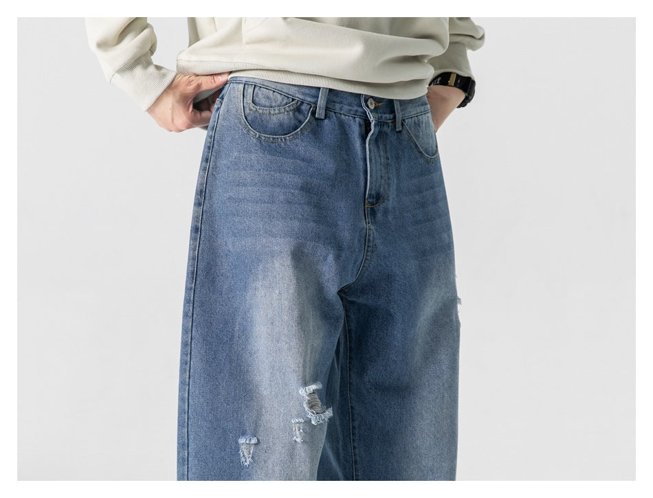 Cropped view of a person wearing blue distressed jeans, showing the front waistband and upper legs.