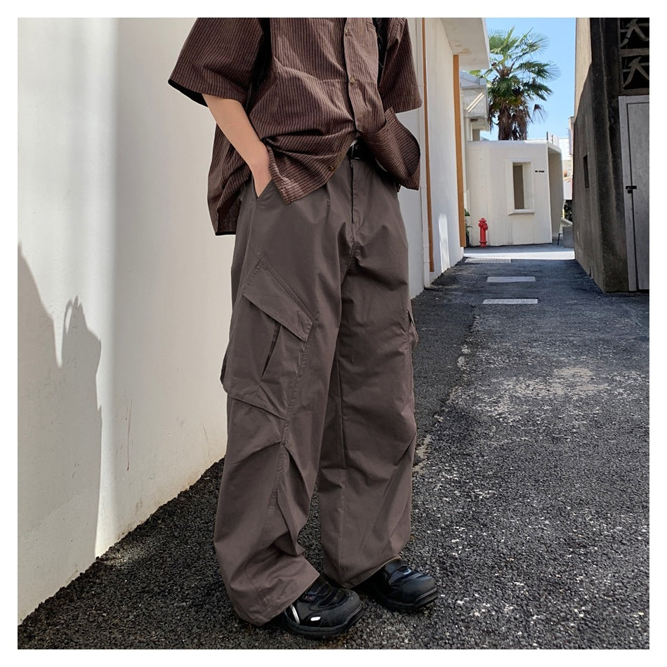 Person wearing brown wide-leg cargo pants with a flap pocket, striped short-sleeve shirt and black sneakers outdoors