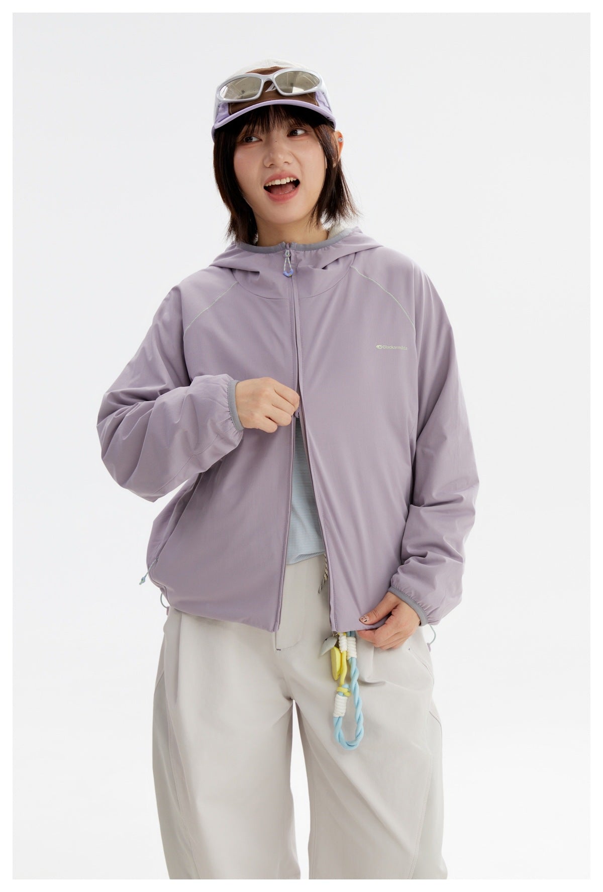 Model wearing a lavender hooded zip jacket, partly unzipped over a pale blue shirt, with off-white trousers.