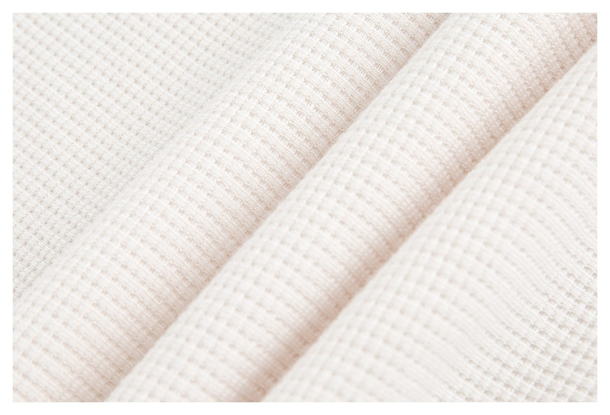 Close-up of pale ivory fabric with a subtle raised grid texture and diagonal folds.