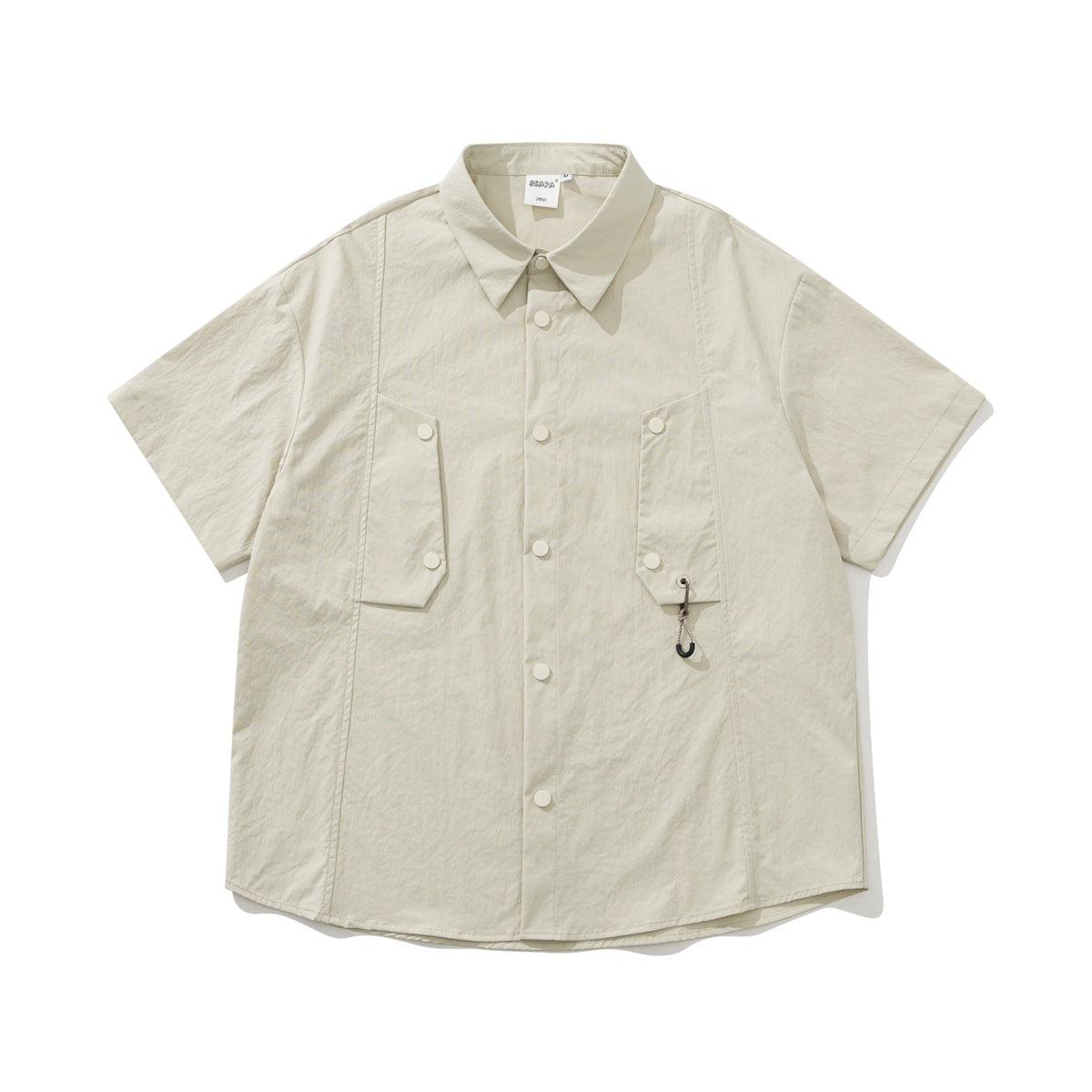 Khaki short-sleeve shirt flat lay with snap front, two flap chest pockets and a small hook charm