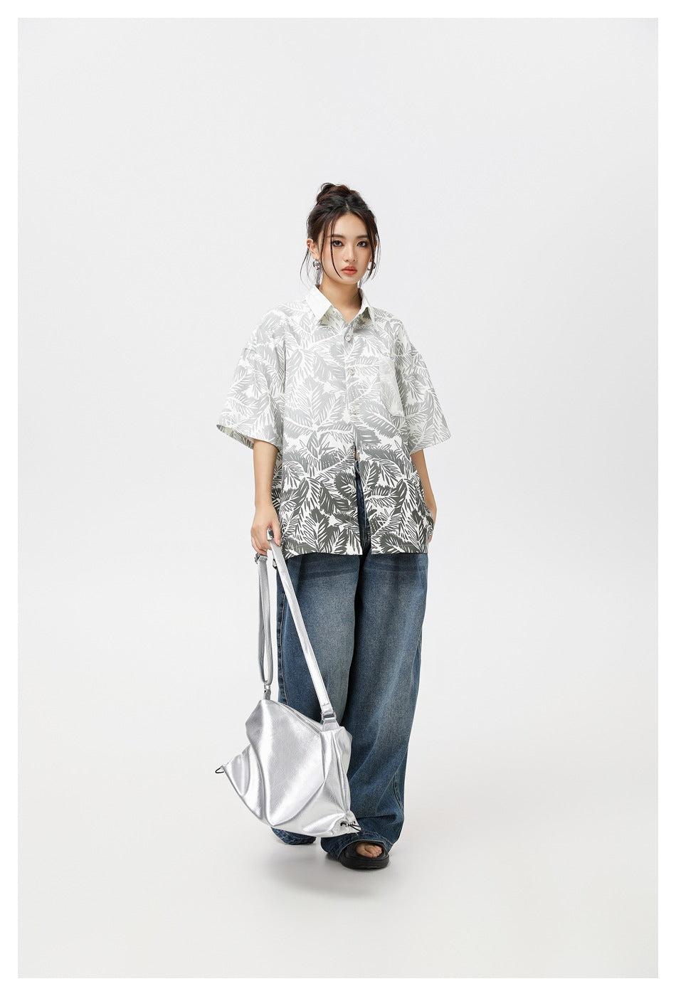Model wearing an oversized white short-sleeve button-up shirt with gray tropical leaf print and blue jeans.