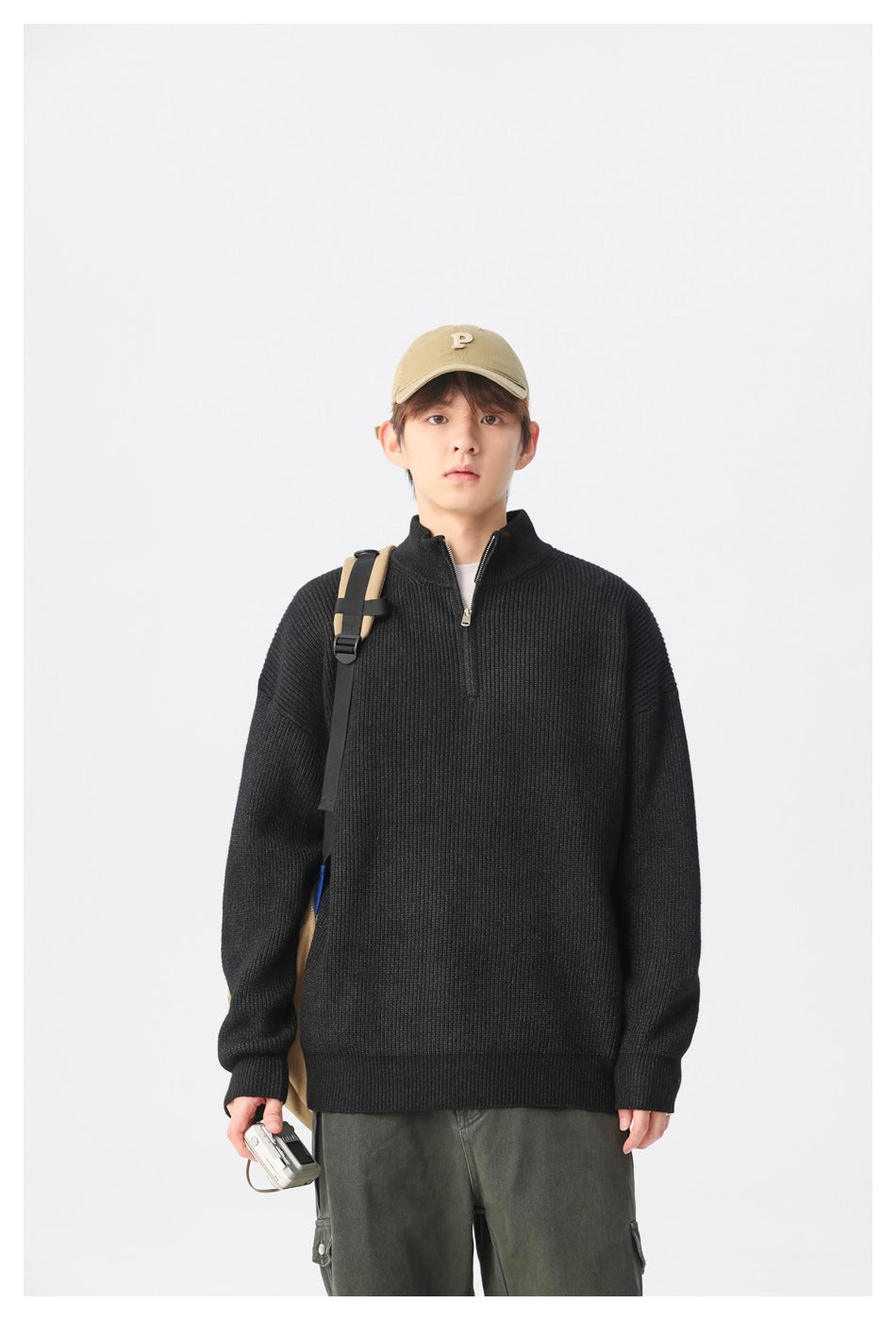 Model wearing a black rib-knit quarter-zip sweater with a tan cap and backpack.