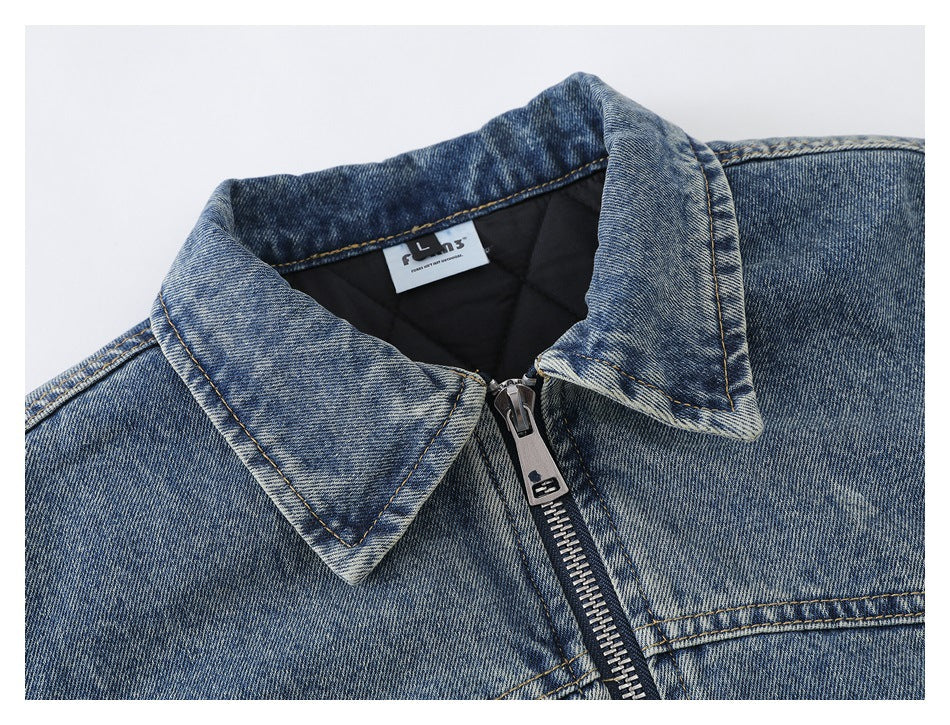Close-up of a blue washed denim jacket collar, black lining, and central metal zipper.