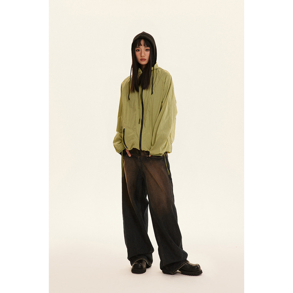 Model wearing an oversized olive-green hooded zip jacket with black drawcords and loose dark jeans.