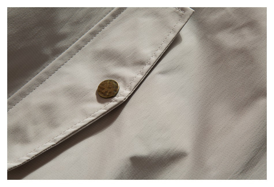 Close-up of a brass-tone button on the light taupe jacket's stitched edge.