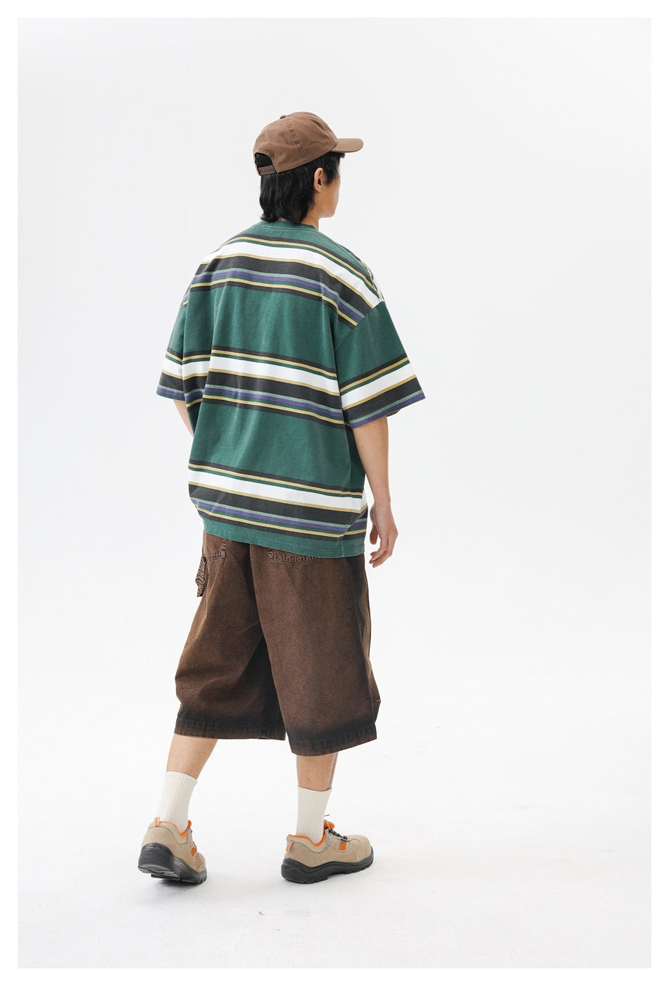 Rear view of a model wearing an oversized forest-green T-shirt with broad white and narrow multicolor horizontal stripes.