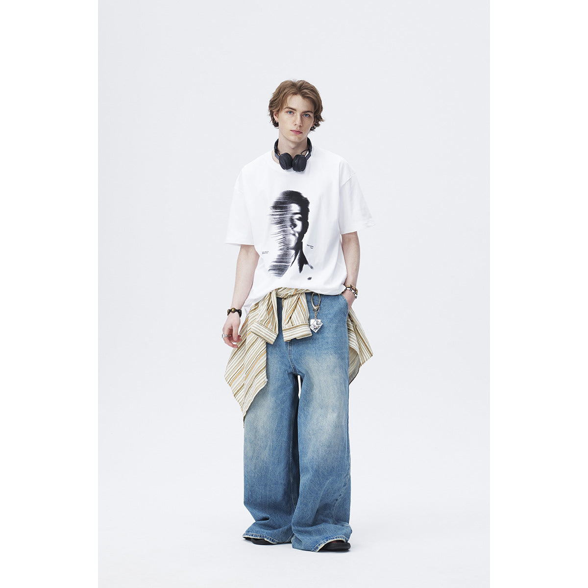 Full-length model wearing a white graphic T-shirt with wide-leg blue jeans and a striped shirt tied at the waist.