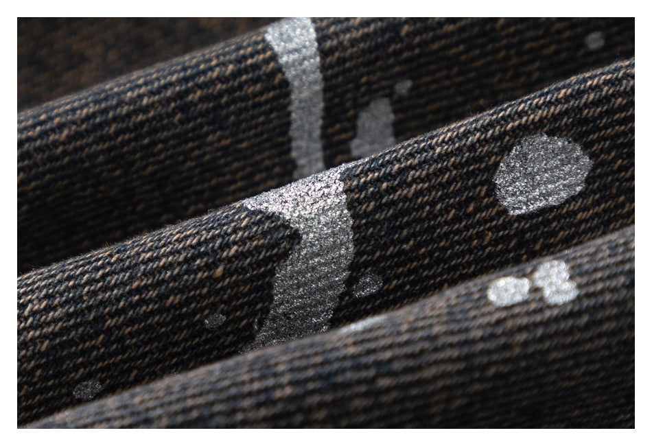 Extreme close-up of dark charcoal woven fabric with scattered irregular silver-gray shapes.