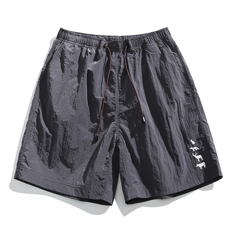 Dark gray crinkled drawstring shorts with elastic waist and small animal embroidery on the lower leg, flat lay