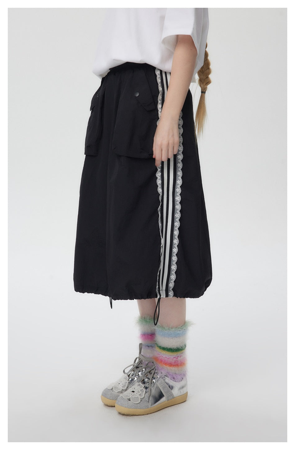 Model wearing the black midi skirt in side view, showing striped lace side trim, flap pockets and drawstring hem