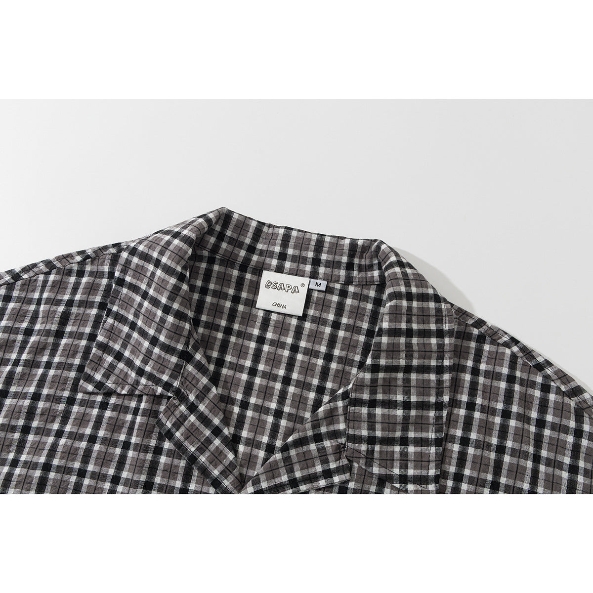 Close-up of a black, gray, and white plaid shirt collar with a visible neck label.