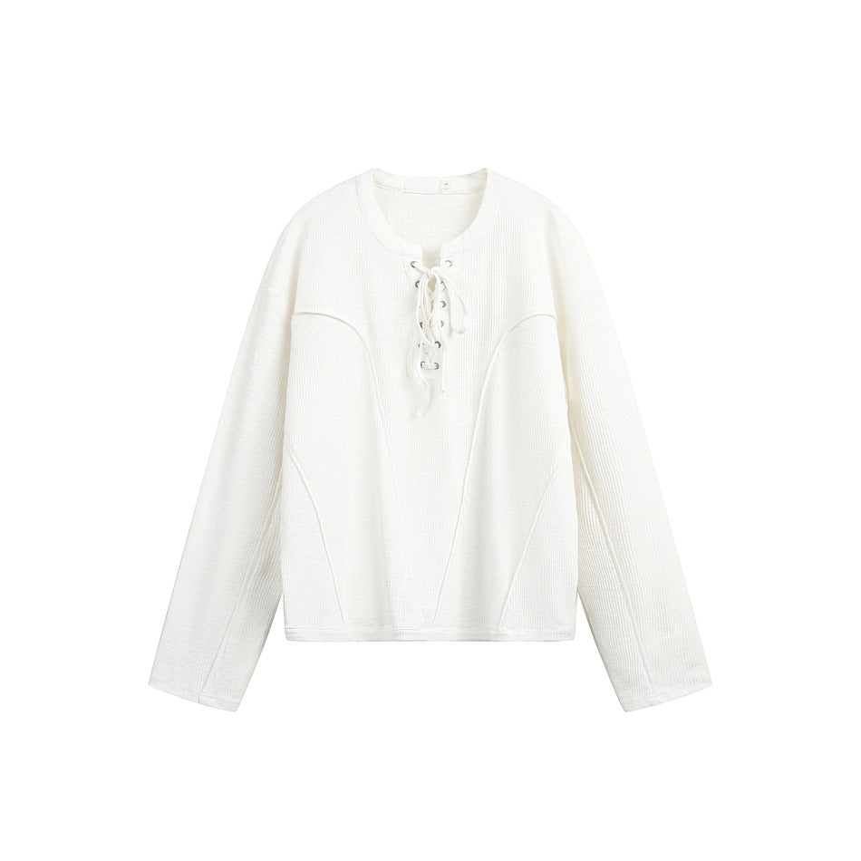 White long-sleeve pullover with lace-up round neckline and curved seams, flat lay on white background