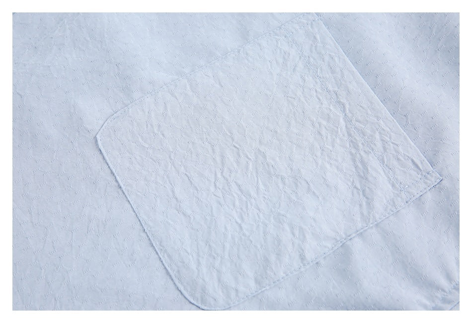Close-up of a light blue shirt's textured fabric and stitched chest pocket.