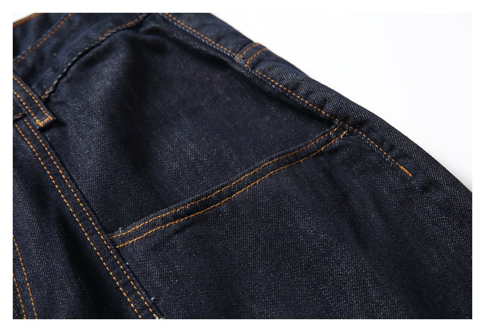 Close-up of dark indigo denim with orange topstitching and a curved pocket seam.