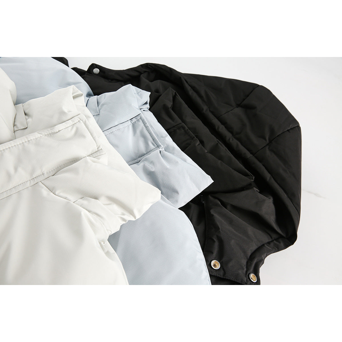 Close-up of white, pale blue, and black padded hooded jackets layered together, showing seams and snap buttons.