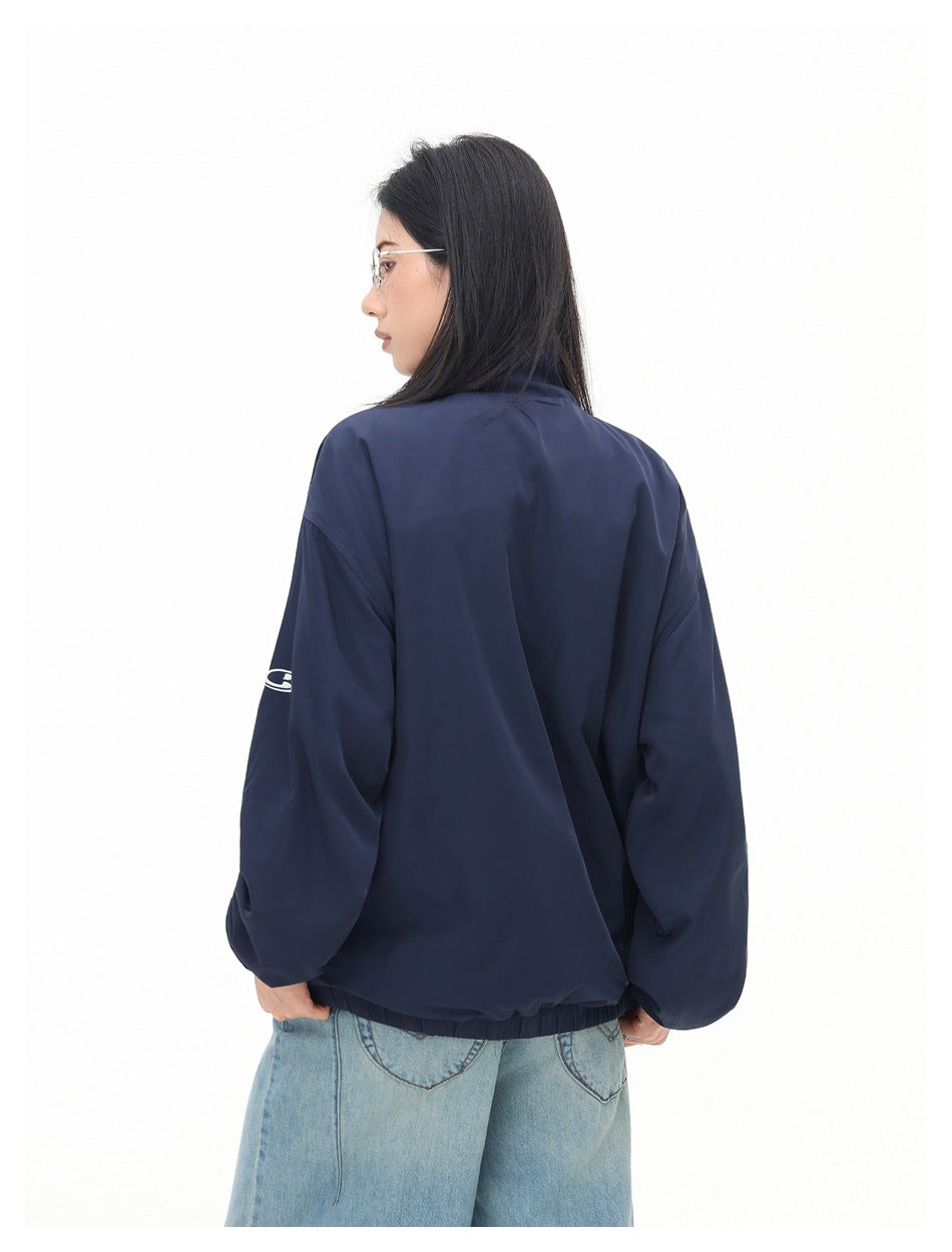 Back view of a model wearing a plain navy jacket with elastic cuffs and hem; a small white sleeve emblem is visible.