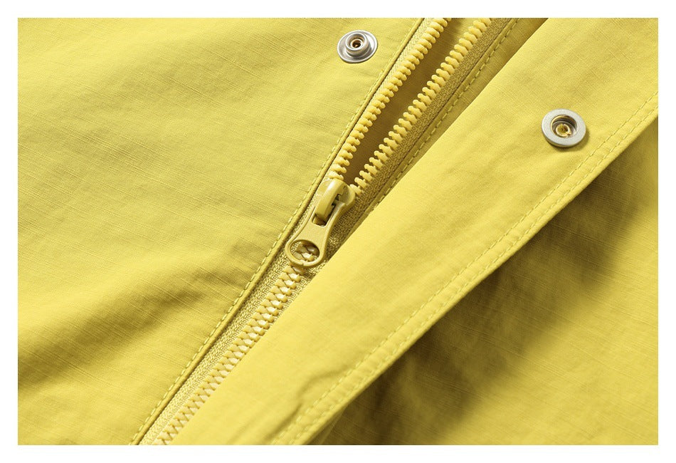 Close-up of a mustard-yellow jacket's front zipper, snap fasteners, and stitched fabric.