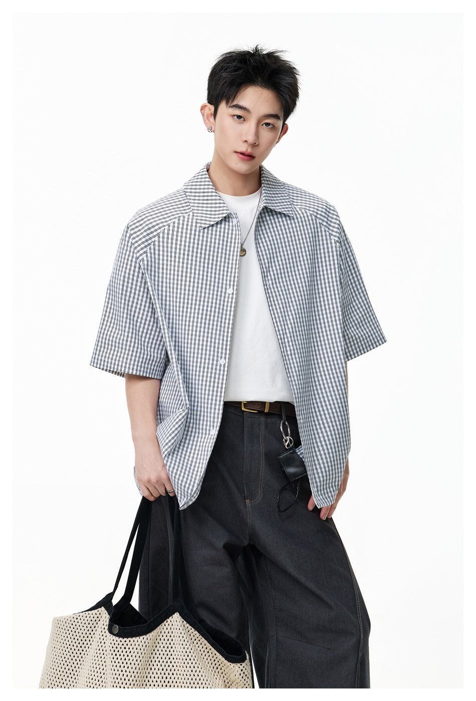 Close-up of a model in an open check short-sleeve shirt over a white tee, holding a mesh tote bag