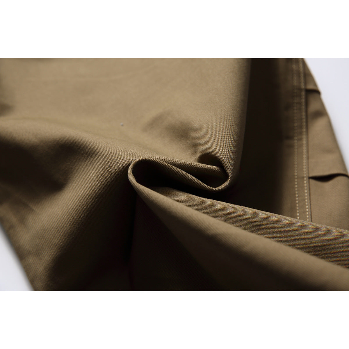 Extreme close-up of olive-brown trouser fabric folded to show its surface and stitching.