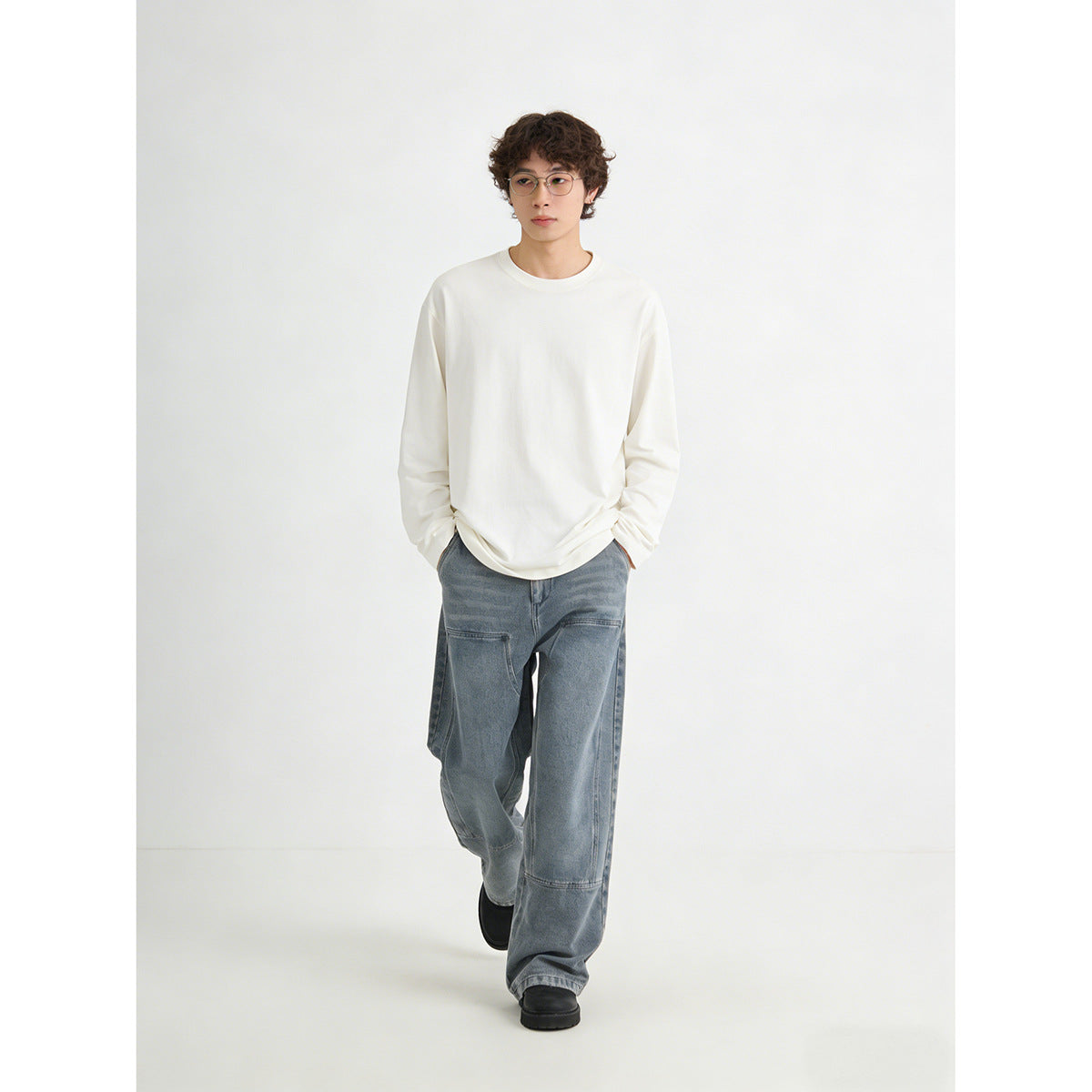 Model wearing an oversized white long-sleeve shirt and loose, washed-blue jeans with large panel pockets.