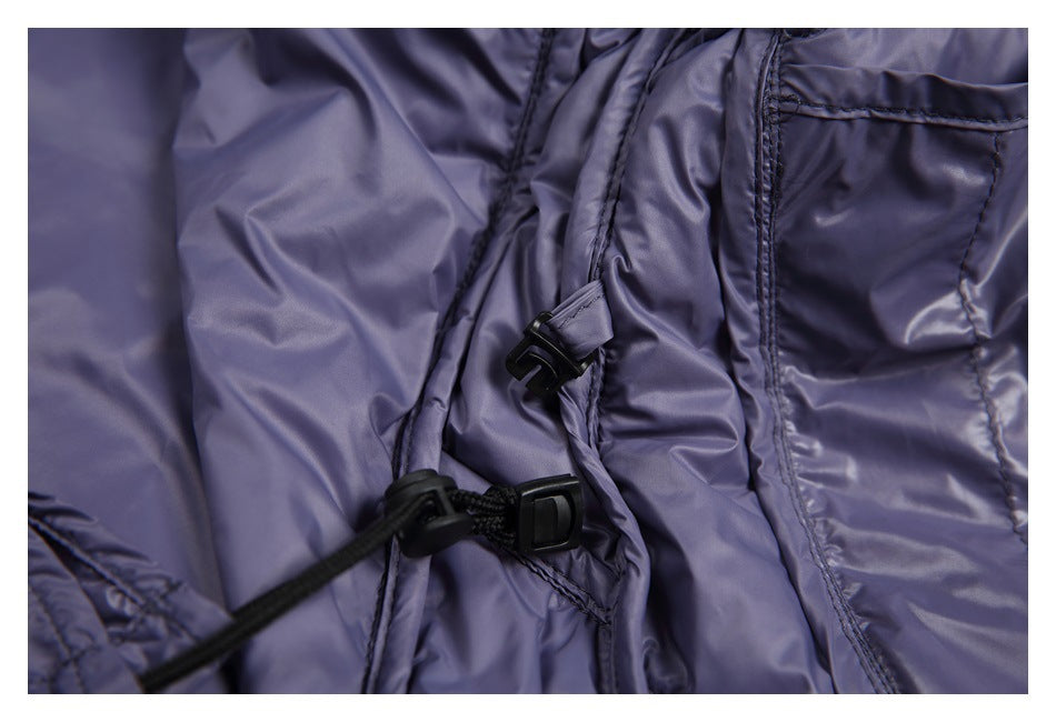 Close-up of black cord locks and an adjustable drawcord beside a pocket on shiny lavender-gray fabric.
