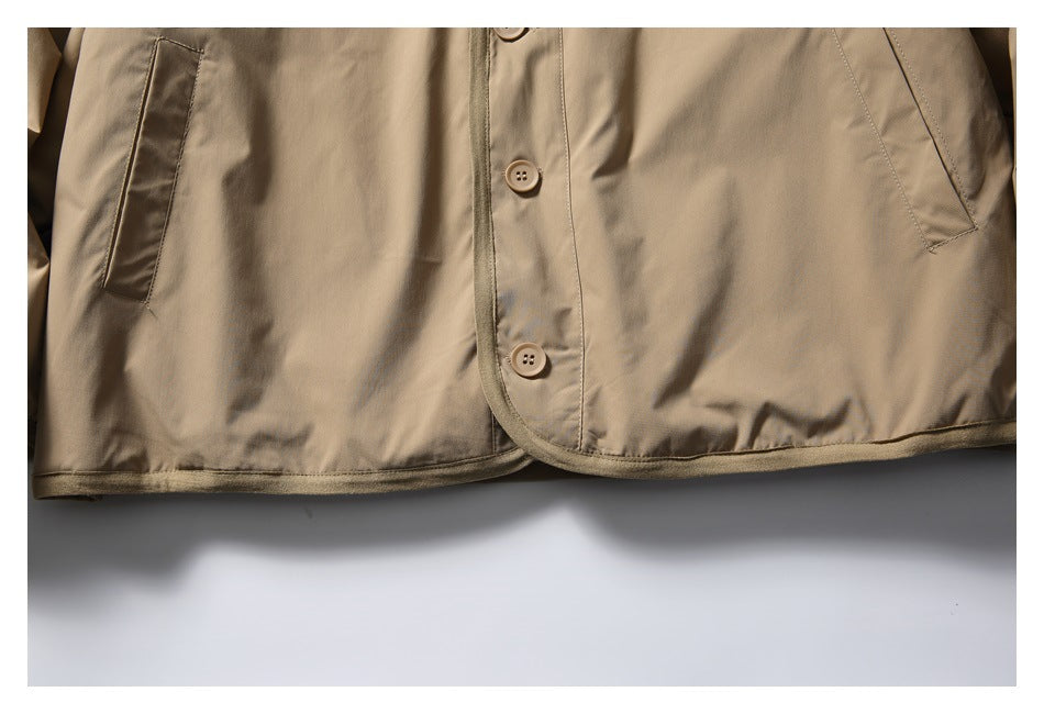 Close-up of the tan jacket's front buttons, angled pockets, seams, and bound hem.