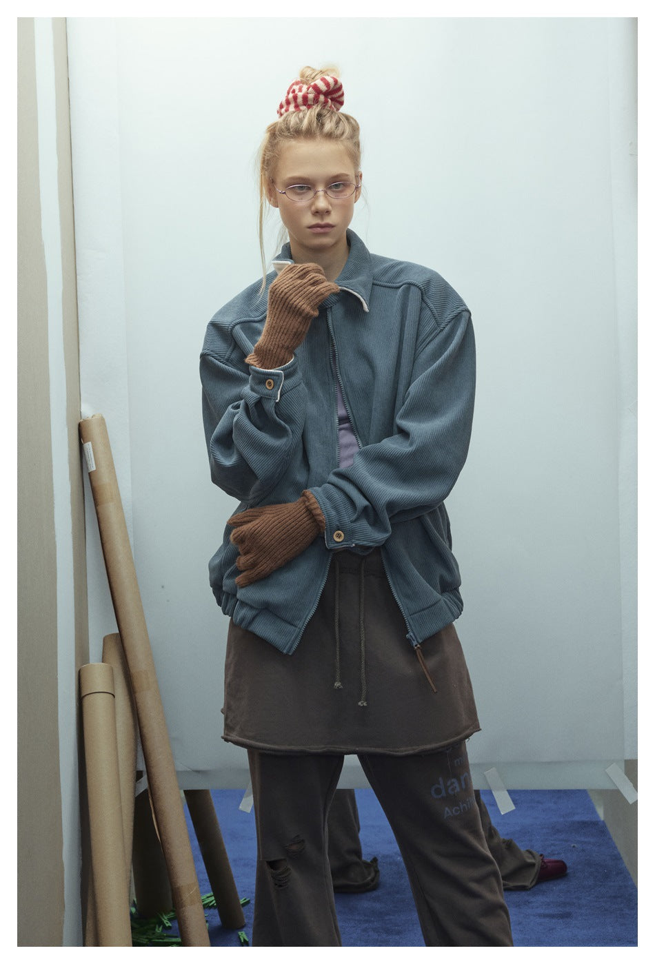 Closer view of a model wearing a blue-gray ribbed jacket with a zip front, high collar, and brown gloves.