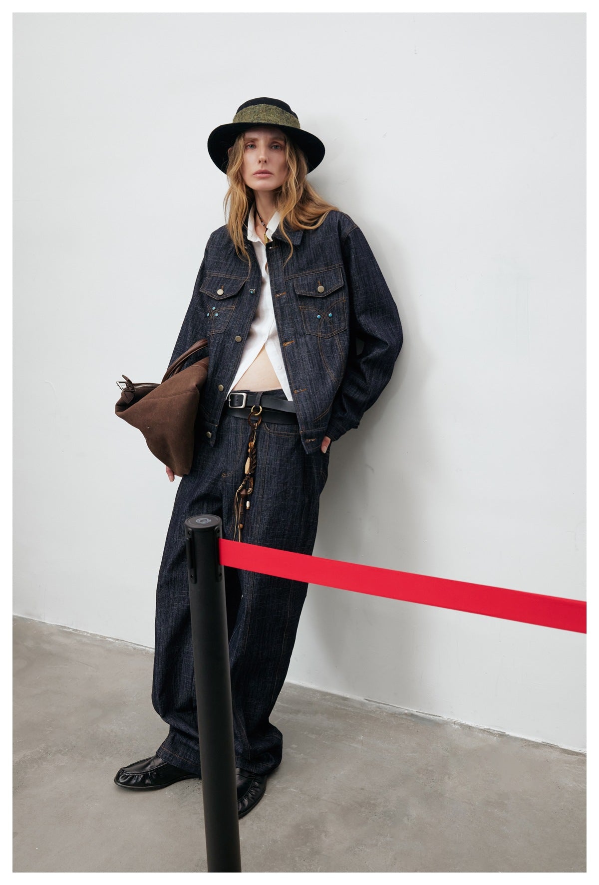 Full-length model wearing a dark indigo denim jacket and matching wide-leg trousers with a white shirt and hat.